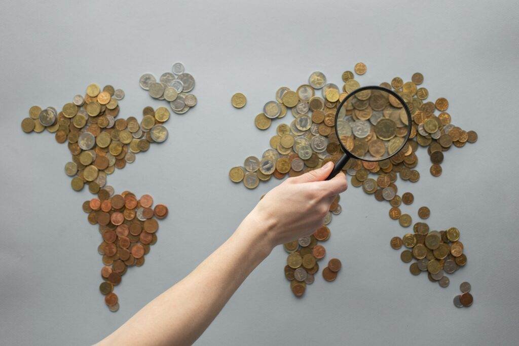 Top view of crop unrecognizable traveler with magnifying glass standing over world map made of various coins on gray background, Best Dividend ETFs for 2023