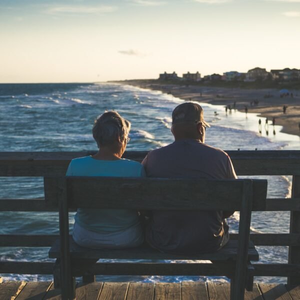 man and woman sitting on bench in front of beach; are dividend stocks best for retirement