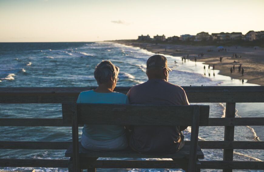 man and woman sitting on bench in front of beach; are dividend stocks best for retirement